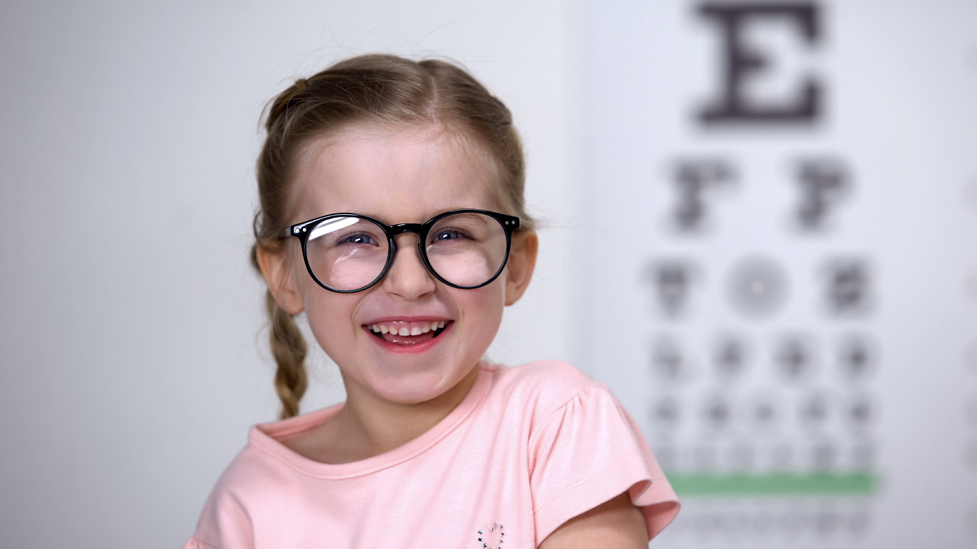 Fille avec lunettes devant planche d'acuité visuelle